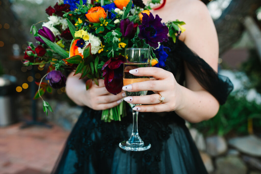 steps for a stress-free los angeles wedding, bride in black wedding dress holding a glass of champagne in her left hand and her bouquet in her right hand cropped tight on her hand and the bouquet.