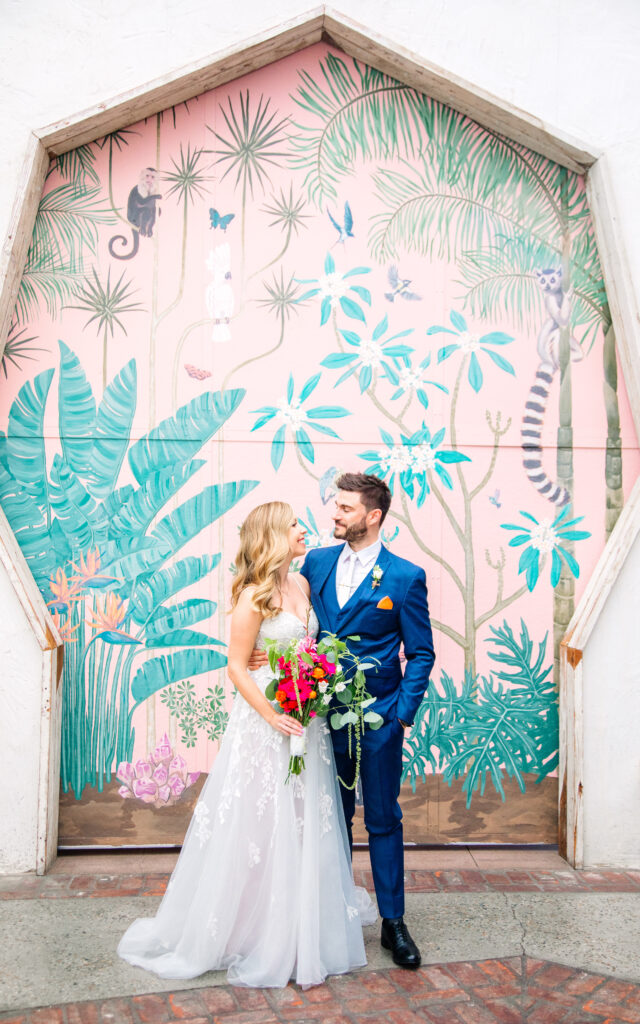 unique los angeles wedding venues, valentine, bride in white and groom in blue in front of tropical pink mural, los angeles wedding photographer