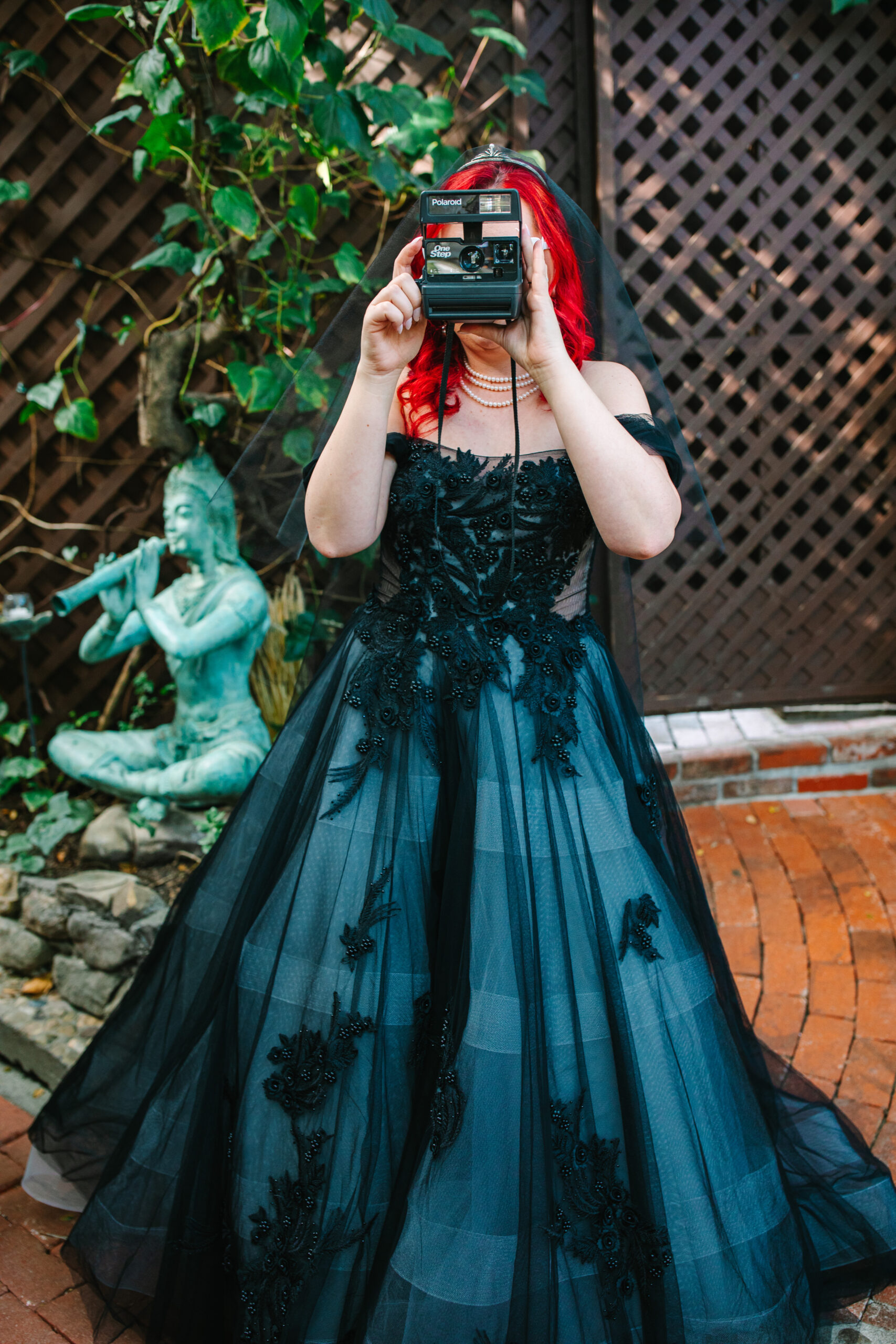 bride with red hair in black wedding dress taking a photo with a polaroid camera