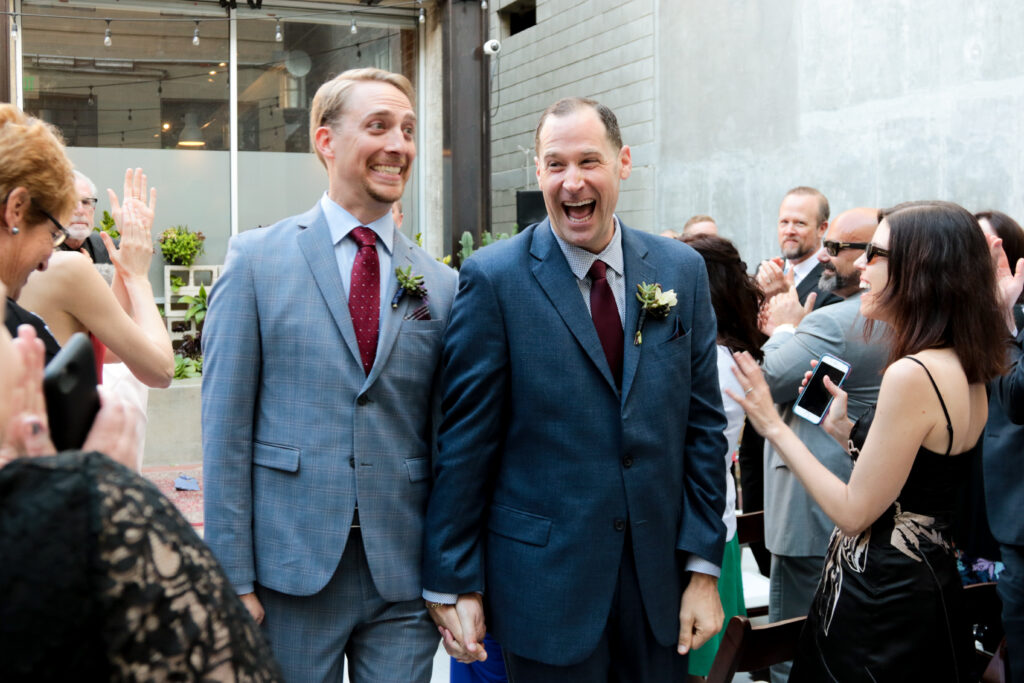 two grooms just married walking back down the aisle with huge smiles on their faces at the gray in long beach. lgbtq+ wedding