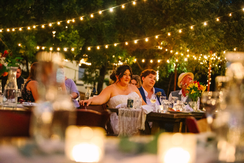 lgbtq+ wedding reception outside after dark with string lights looking at the brides