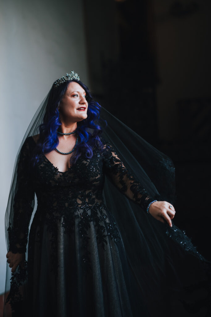 black wedding dress, woman standing in a black lace wedding dress with purple hair and a jeweled crown.