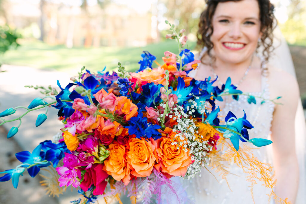 Colorful wedding bouquet, orange pink and blue bridal bouquet held by a smiling bride in white 