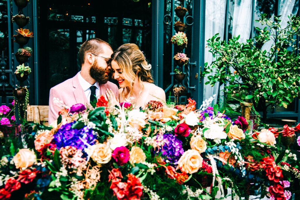 wedding photographer in los angeles, bride and groom at colorful sweetheart table snuggling groom in pink suit and bride in white