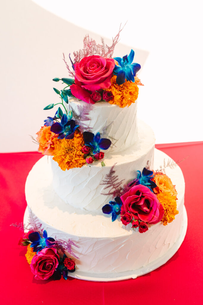 white wedding cake with bright orange pink and blue flowers placed on it. colorful wedding