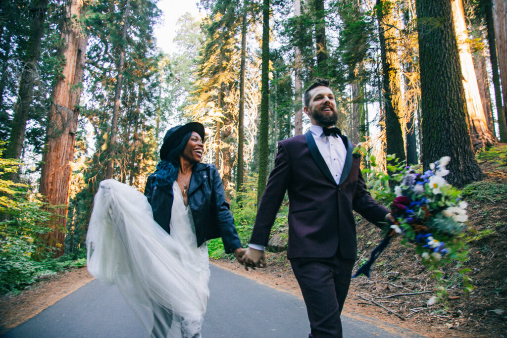 candid wedding photography, bride and groom running down the middle of a road in a forest in sequoia