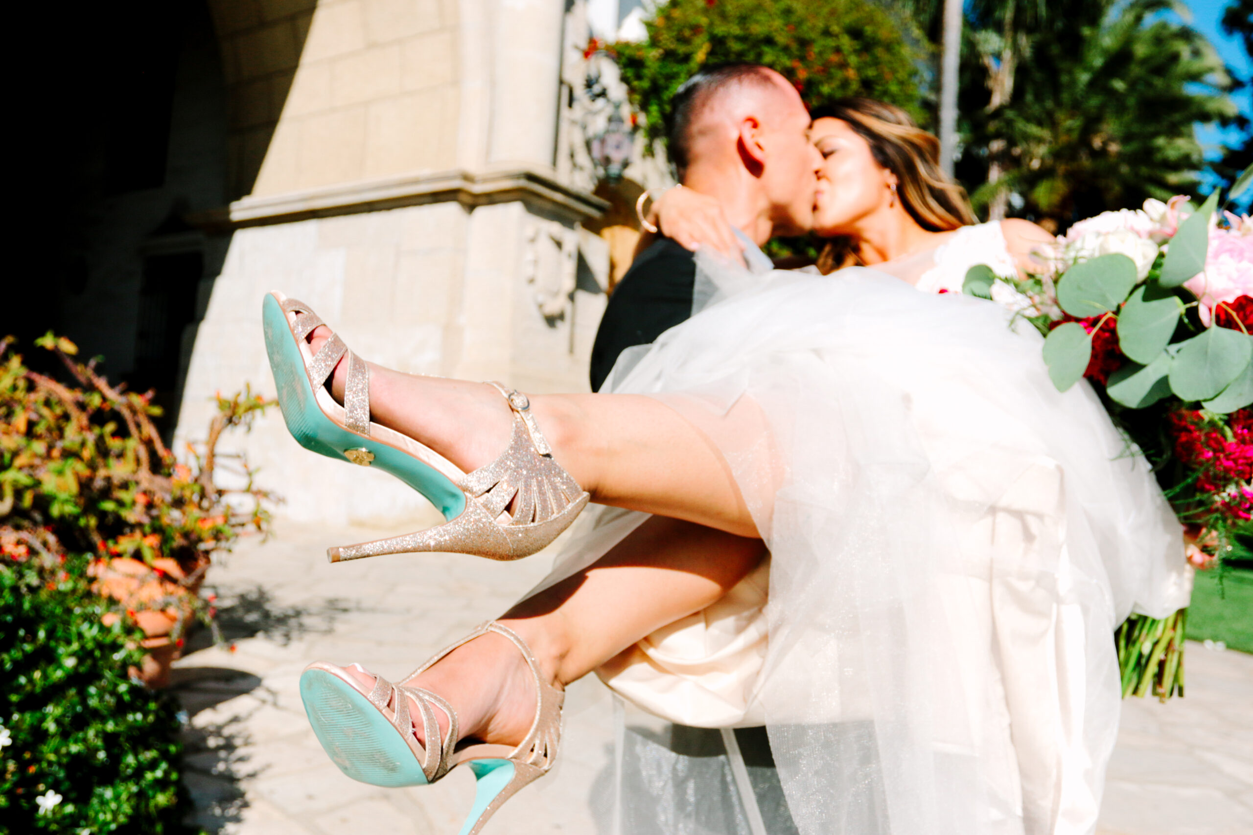 Candid wedding photography, groom carrying bride in with her gold heels in focus at the santa barbara courthouse