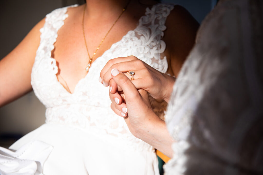 candid wedding photography, brides holding hands in the sun, but all you can see is their hands and one of the brides upper body.