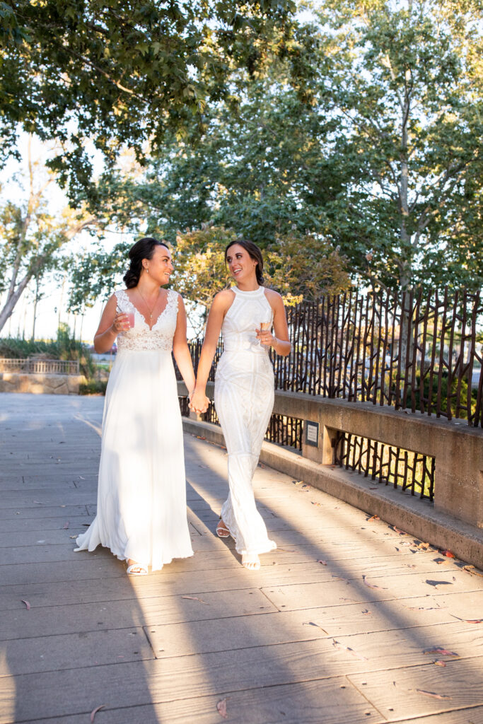 two brides in white wedding dresses walking hand in hand.