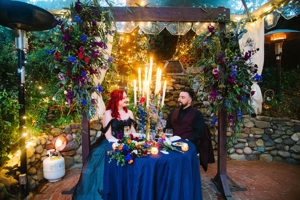 Inn of the Seventh Ray Wedding, bride and groom at their sweetheart table framed by the arch adorned with flowers that they got married under.