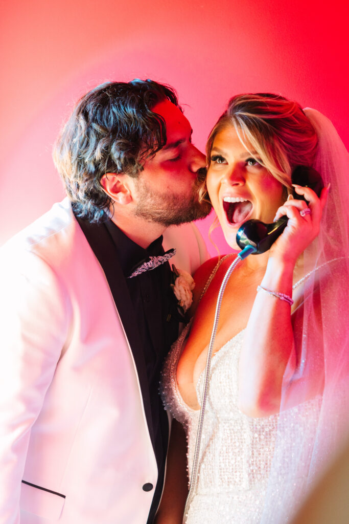 Madonna Inn Wedding, bride and groom portraits by a telephone, bathed in pink light.