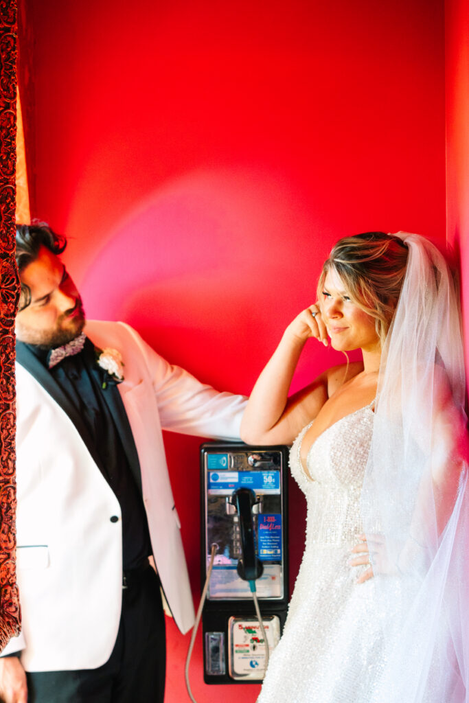 Madonna Inn Wedding, bride and groom portraits by a telephone, bathed in pink light.