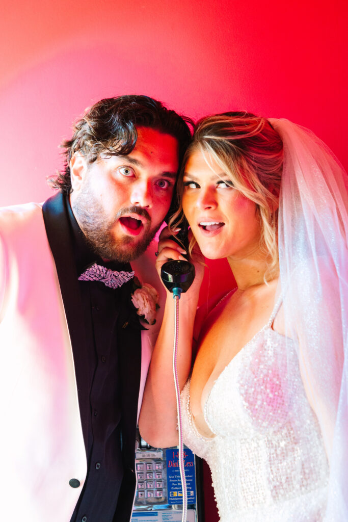 Madonna Inn Wedding, bride and groom portraits by a telephone, bathed in pink light.